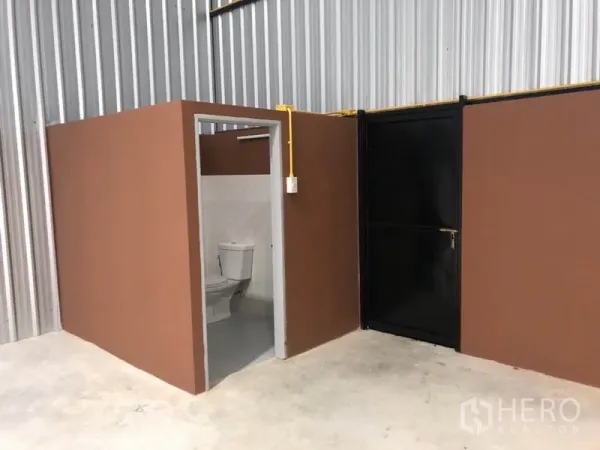 Warehouse for rent in Khlong Luang, Pathum Thani - Internal restroom and black service door inside the warehouse unit.