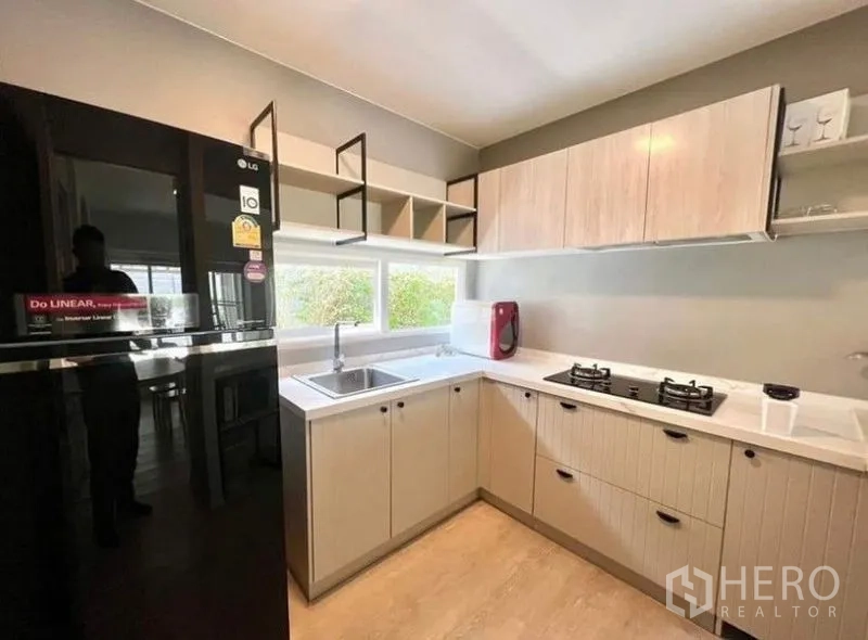 Detached House for rent - U-shaped modern kitchen with gas hob, light wood cabinetry and large black refrigerator.