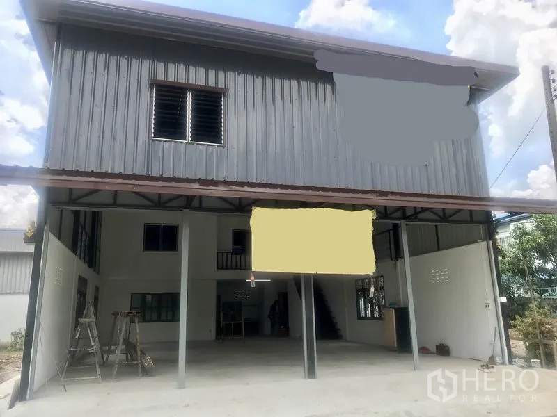 货栈 出租在Lam Luk Ka, Pathum Thani - 两层钢板外墙仓库外观，前方带有遮棚装卸区与停车位