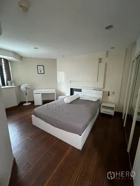Condominium for rent - Corner bedroom with wood flooring, white bed frame and mirrored wardrobe.