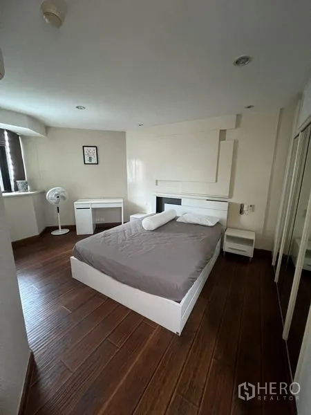 Condominium for rent - Corner bedroom with wood flooring, white bed frame and mirrored wardrobe.