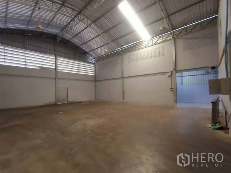 Factory for rent or sale in Mueang Samut Sakhon, Samut Sakhon - Spacious high-ceiling warehouse hall with ventilation panels and concrete floor.