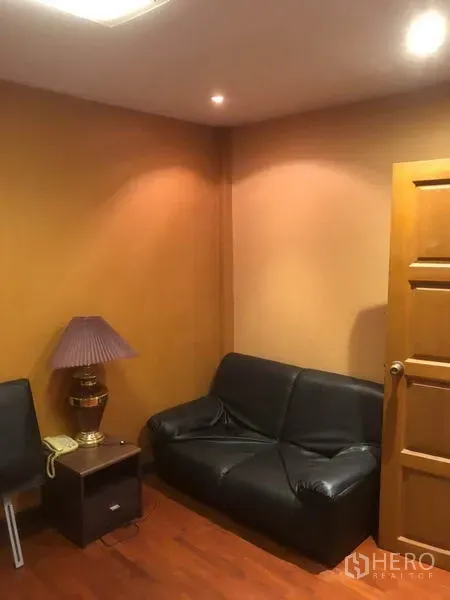 Shophouse for rent in Bang Rak, Bangkok - Compact sitting area with black leather sofa and side table in a warm-toned room.