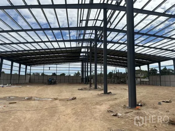 Warehouse for rent or sale in Nikhom Phatthana, Rayong - Interior shot showing open-span steel columns and roof framing over compacted ground in the warehouse.