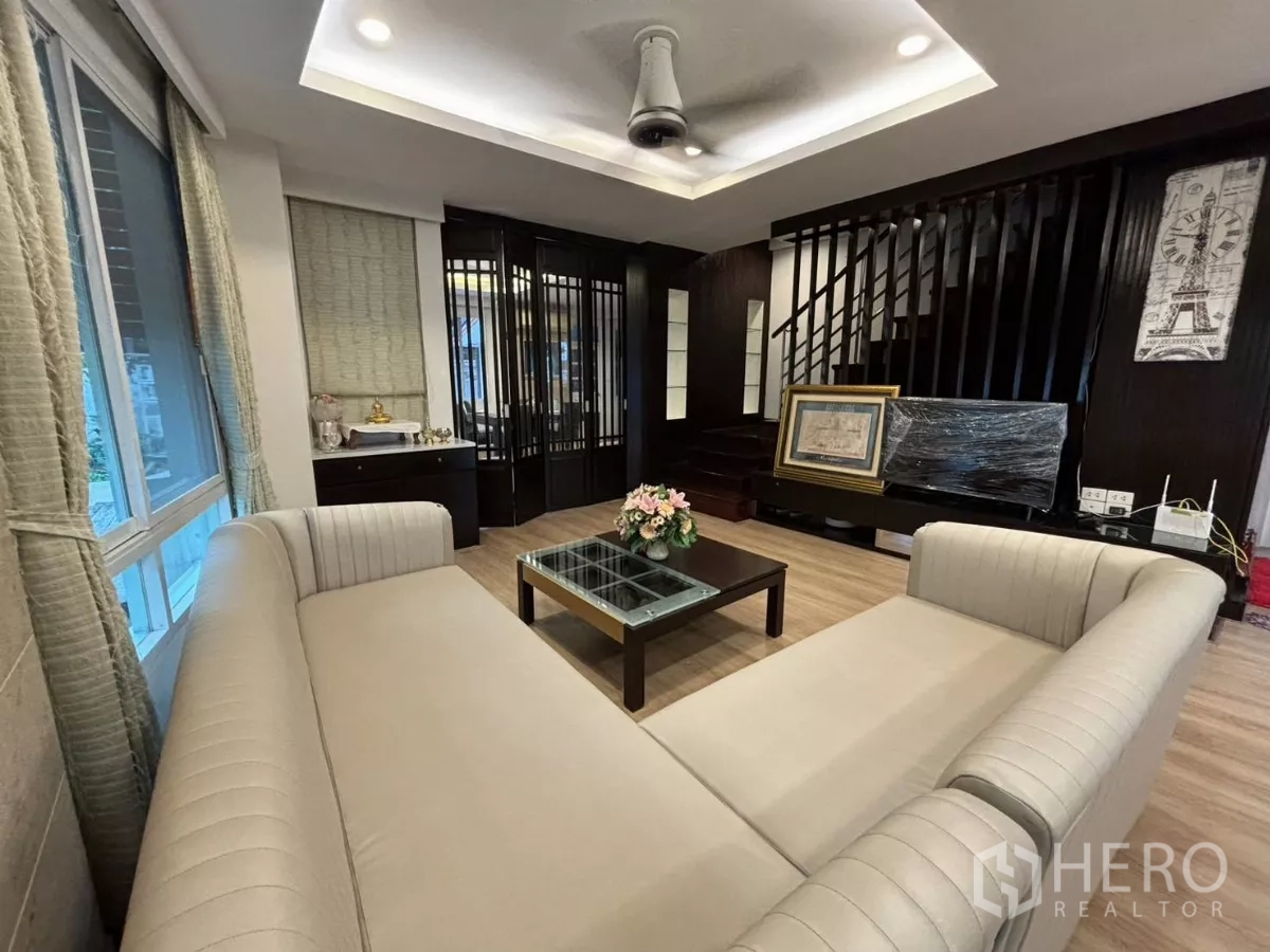 Detached House for rent in Bang Kapi, Bangkok - Cozy lounge with beige sofas, staircase, and dark wood accents.