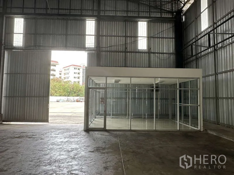 Warehouse for rent in Pak Kret, Nonthaburi - Interior entry showing tall sliding door and a glass-partition office facing the yard.