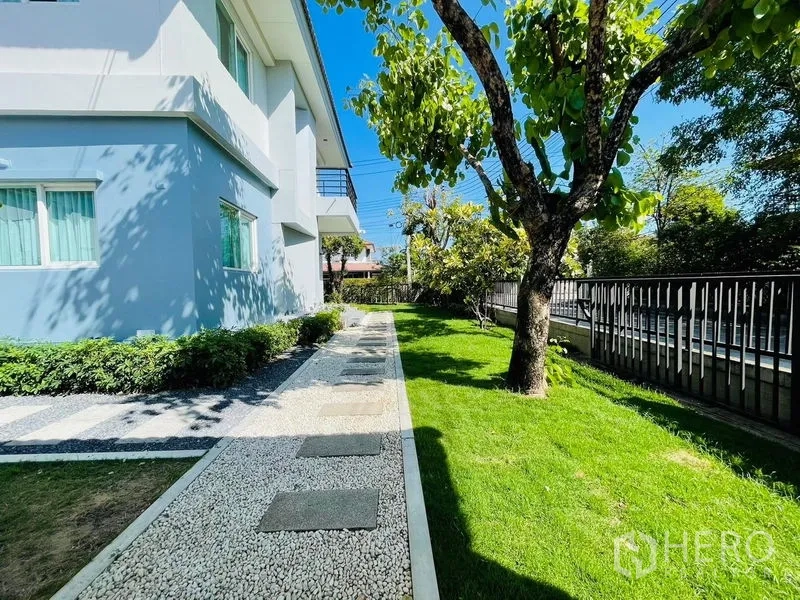 Detached House for sale in Lam Luk Ka, Pathum Thani - Side garden with gravel walkway along the house and a shady tree.
