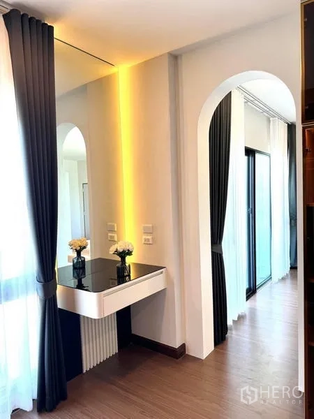 Detached House for rent or sale in Bang Phli, Samut Prakan - Vanity corner with backlit mirror beside an arched hallway and glass sliding doors with curtains.