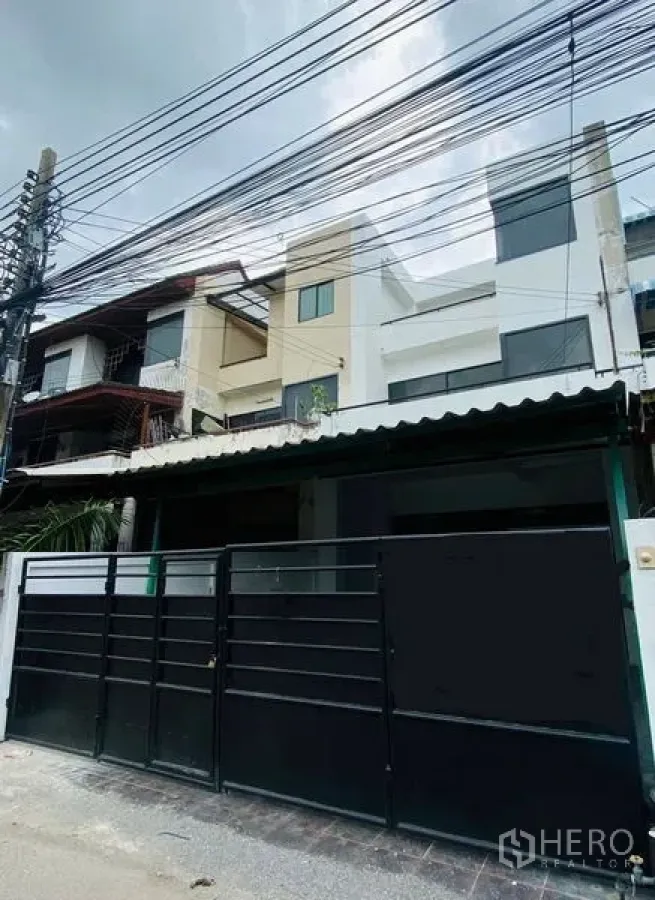 Home Office for rent or sale in Suan Luang, Bangkok - Street view of a three-storey home office with a black metal gate and overhead cables.