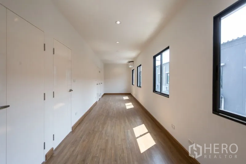 Townhouse for rent in Bang Phli, Samut Prakan - Bright upper corridor with wood flooring, white built‑in doors and black-framed windows.