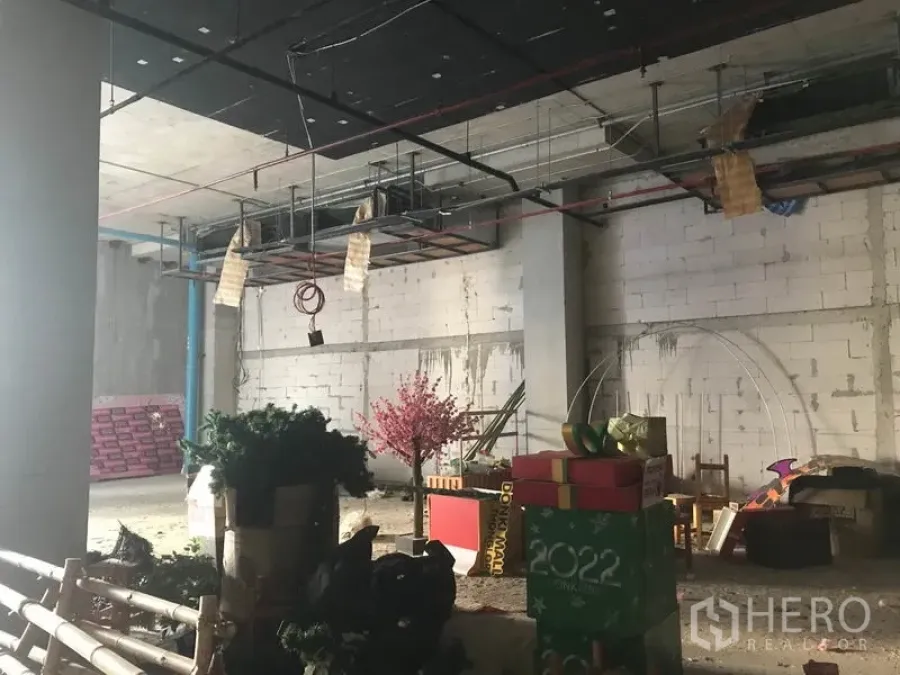 零售空间 出租在Khlong Toei, Bangkok - 未装修店铺全景，悬挂管道、混凝土柱与临时装饰品。