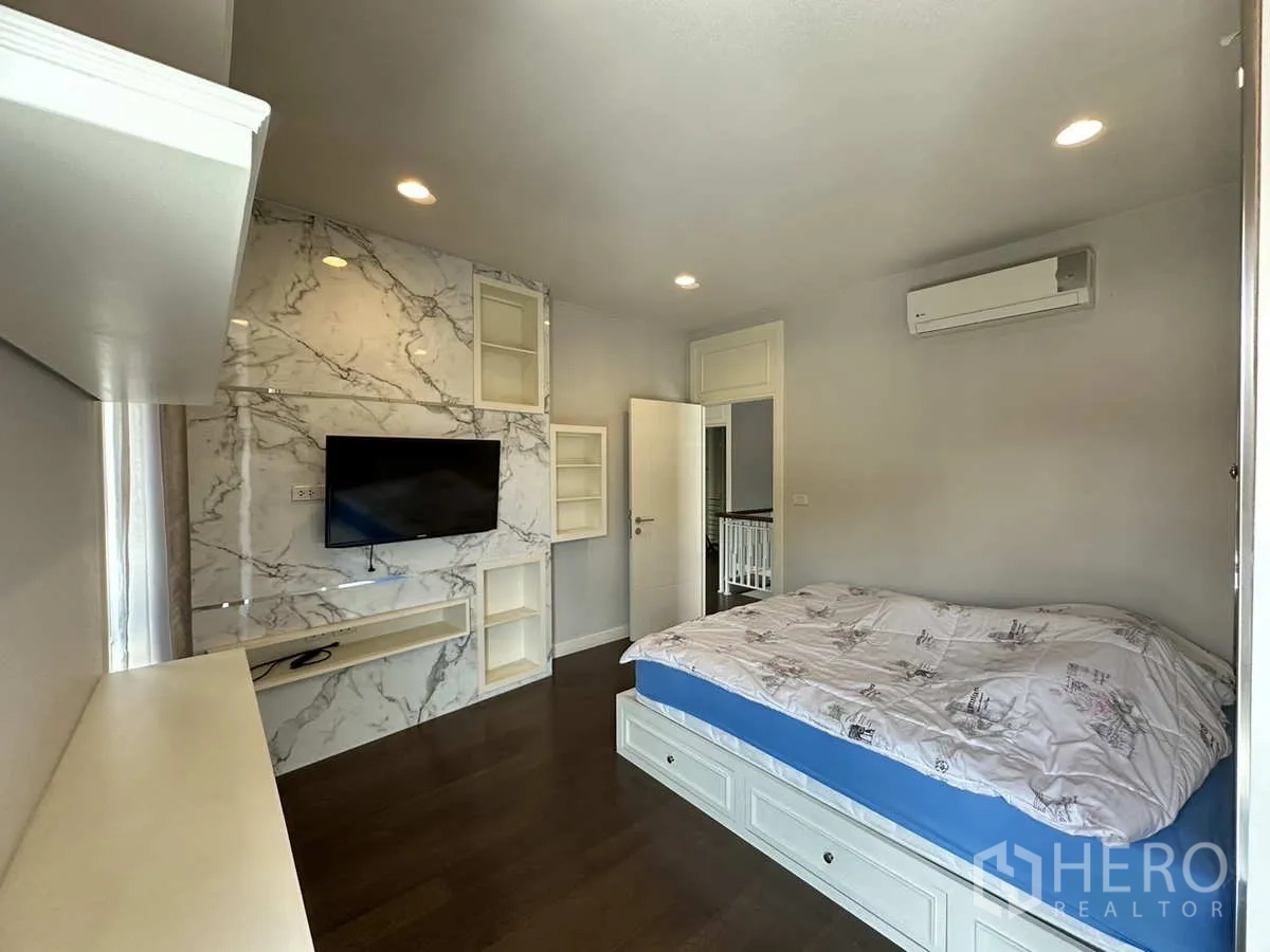 Detached House for rent or sale in Lam Luk Ka, Pathum Thani - Bedroom with marble feature wall, mounted TV and built-in shelves.