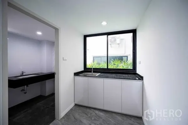 Home Office for rent in Suan Luang, Bangkok - Compact pantry with black countertop and window, with a doorway to a restroom beside it.