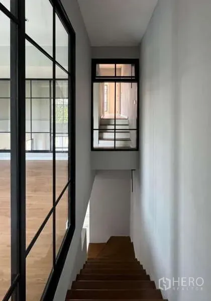 Townhouse for rent or sale in Prawet, Bangkok - Wood staircase and hallway with black-framed glass partitions.