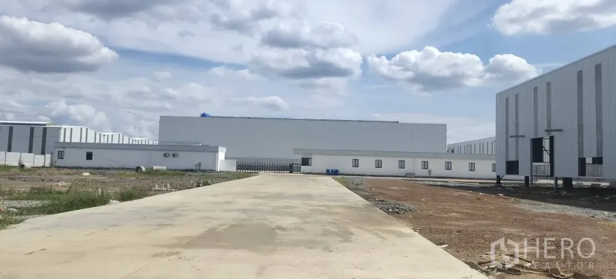 Factory for rent in Plaeng Yao, Chachoengsao - Wide concrete driveway leading to a large warehouse and a low-rise building wing.