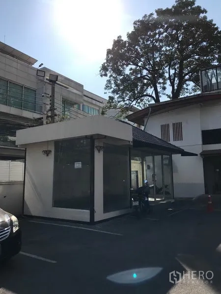 Retail Space for rent in Watthana, Bangkok - Angle view of compact glass-box retail building with parking lot and mature tree.
