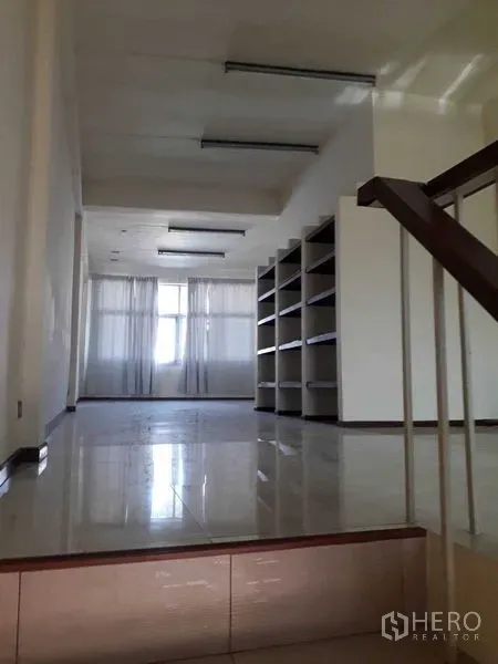 Shophouse for rent in Suan Luang, Bangkok - Raised landing and staircase leading to a spacious bright room with shelving and sheer curtains.