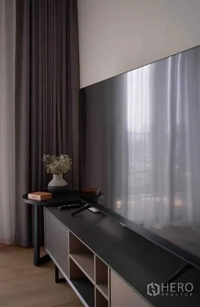 Condominium for rent or sale in Khlong Toei, Bangkok - Large flat-screen TV on a modern console beside floor-to-ceiling curtains.