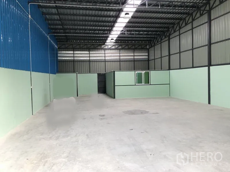 Warehouse for rent in Nonthaburi - Spacious 300 sqm warehouse interior featuring high steel truss roof, skylight strip and concrete floor with a built-in office.