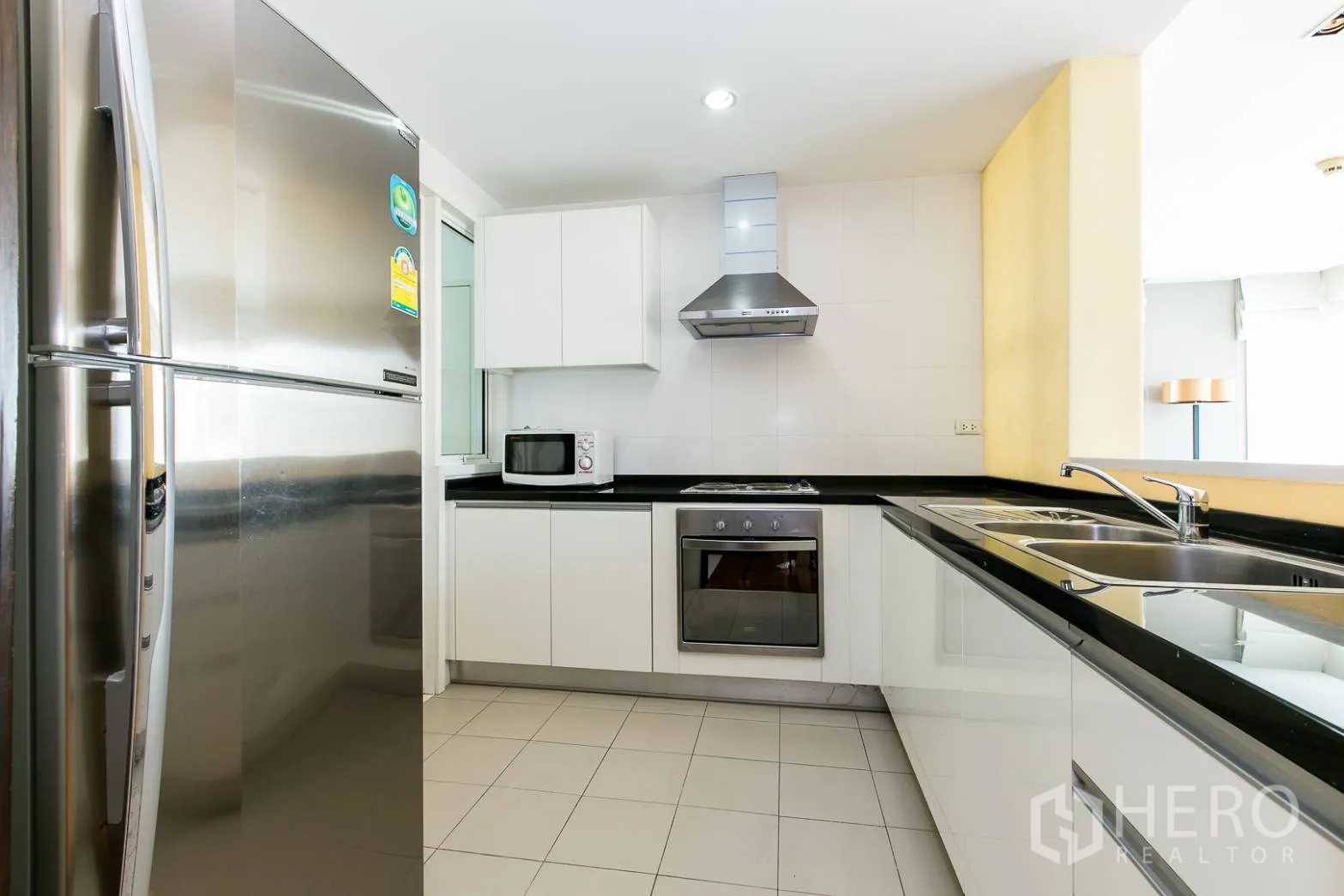 Condominium for rent or sale in Khlong Toei, Bangkok - U-shaped kitchen with white cabinets, black countertops and stainless appliances.