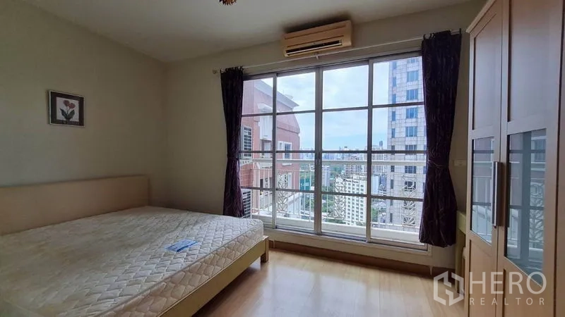 Condominium for rent in Khlong Toei, Bangkok - Second bedroom with large window, city view, air conditioner, and light wood wardrobe.