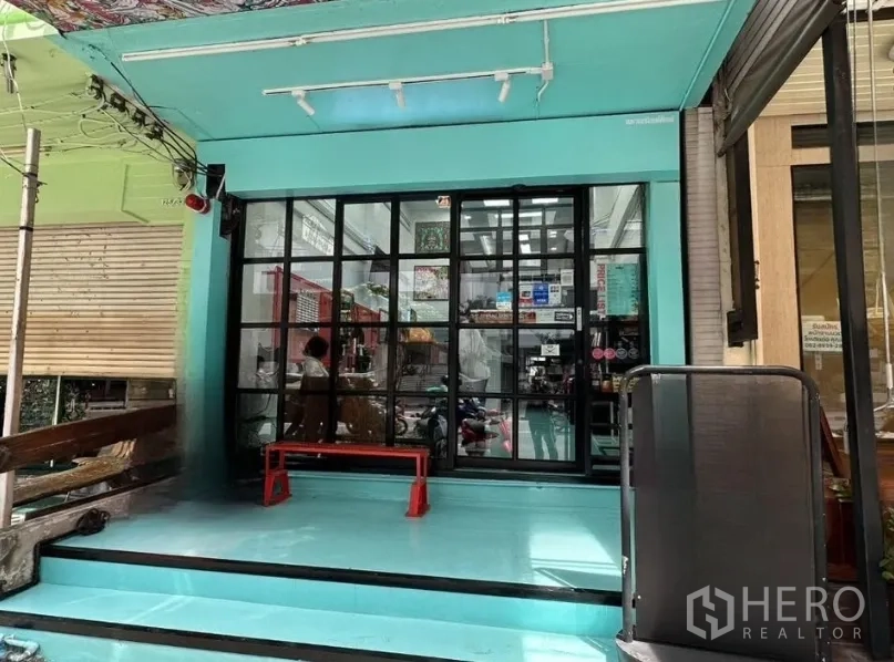 Shophouse for sale in Watthana, Bangkok - Turquoise shophouse frontage with black-framed glass doors and raised entry steps on Sukhumvit.