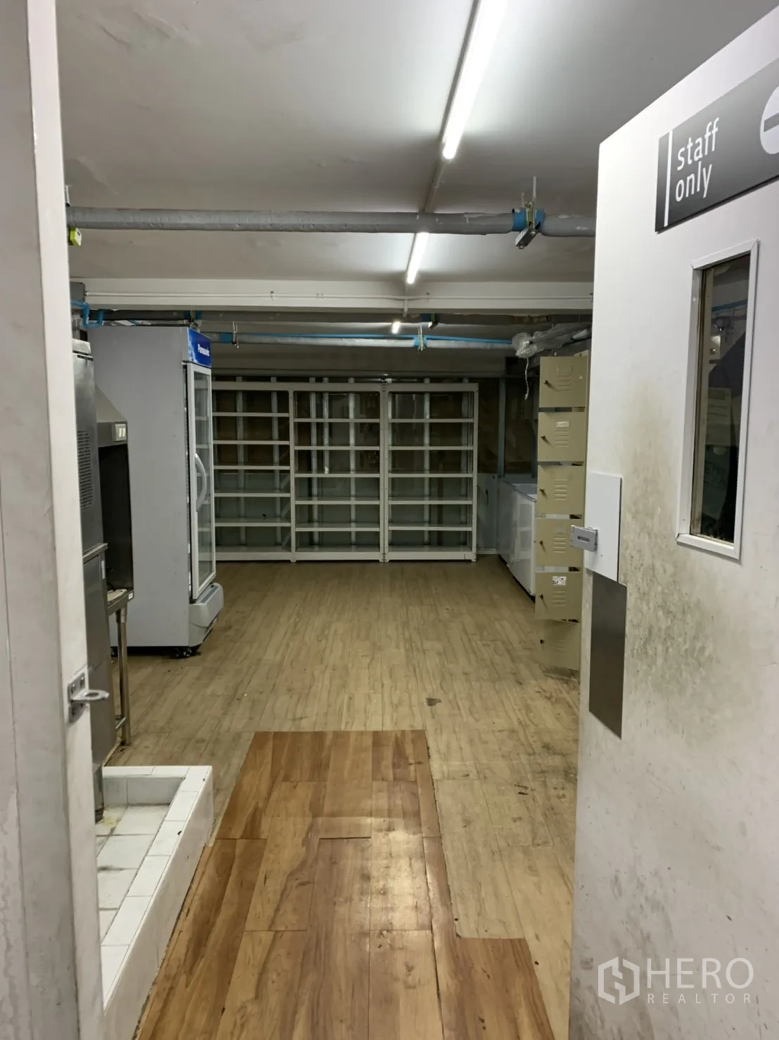 Retail Space for rent in Sathon, Bangkok - View through a staff-only doorway to a stock room with wood-look floors, refrigerators and wall shelving.