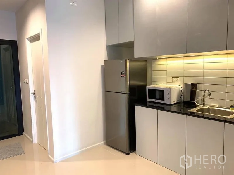 Home Office for rent - Compact pantry with black countertop, sink, microwave and stainless-steel refrigerator.