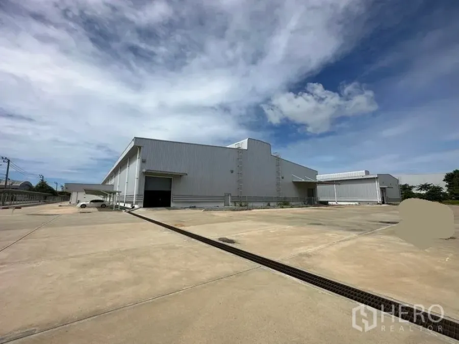 Factory for rent in Bang Sao Thong, Samut Prakan - Modern steel-clad factory exterior with a wide concrete yard and loading bay under blue sky.