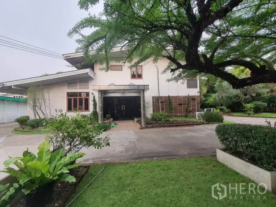 Home Office for rent in Watthana, Bangkok - Front of two‑storey home office with lawn and driveway in a green compound