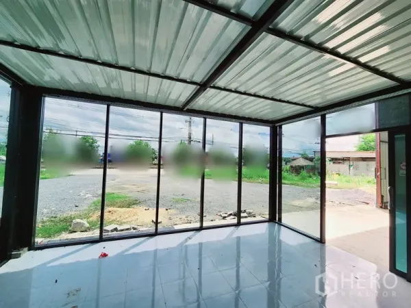 Warehouse for rent in Sam Phran, Nakhon Pathom - Glass-front office area of the warehouse with floor-to-ceiling windows overlooking a wide gravel yard and greenery.