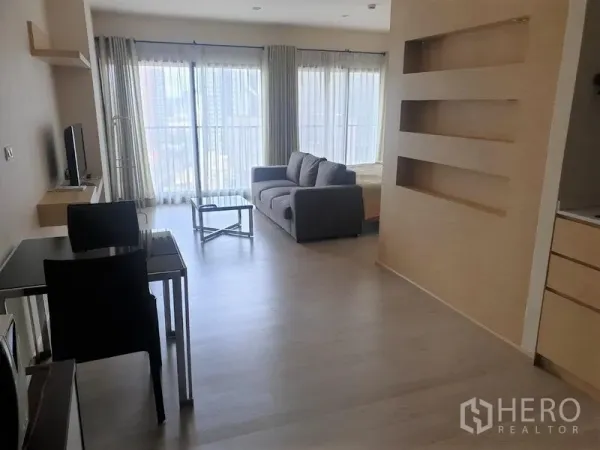 Condominium for rent in Khlong Toei, Bangkok - Open-plan living area with floor-to-ceiling windows, gray sofa, glass coffee table, TV and balcony city view.