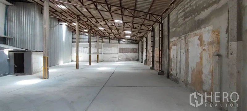Warehouse for rent in Phra Khanong, Bangkok - Long warehouse bay with high clear span, corrugated metal side wall, and smooth concrete slab flooring.