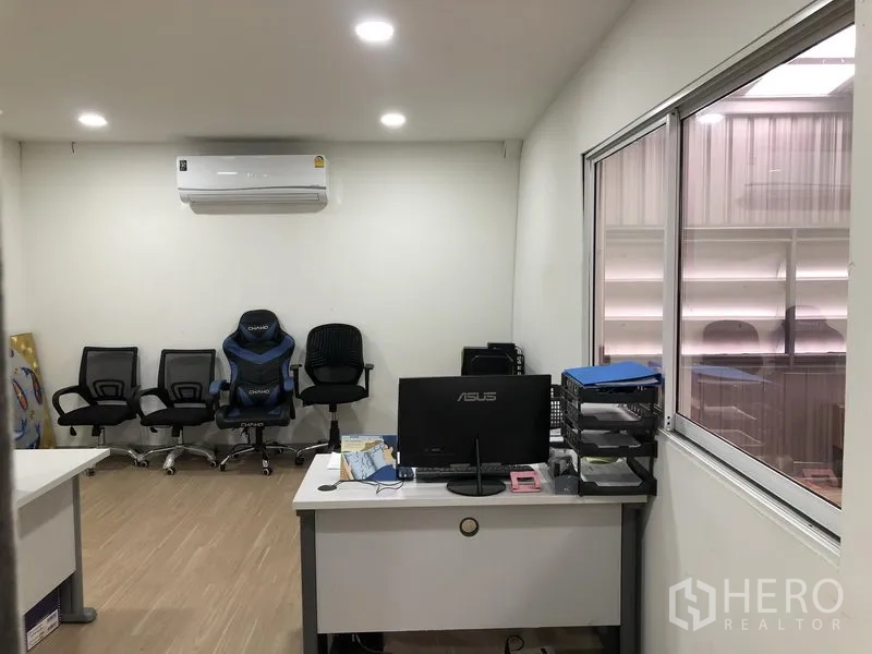 Warehouse for rent in Nonthaburi - Compact office with desk, task chairs, window to warehouse and wall-mounted air conditioner.