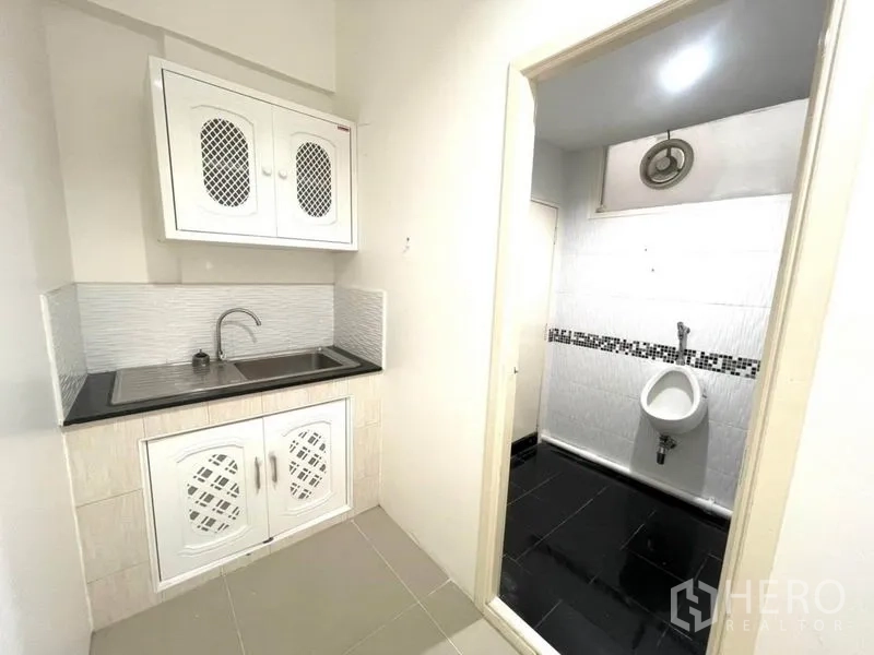 Office Space for rent in Khlong Toei, Bangkok - Compact pantry with sink and cabinetry beside the restroom entrance.