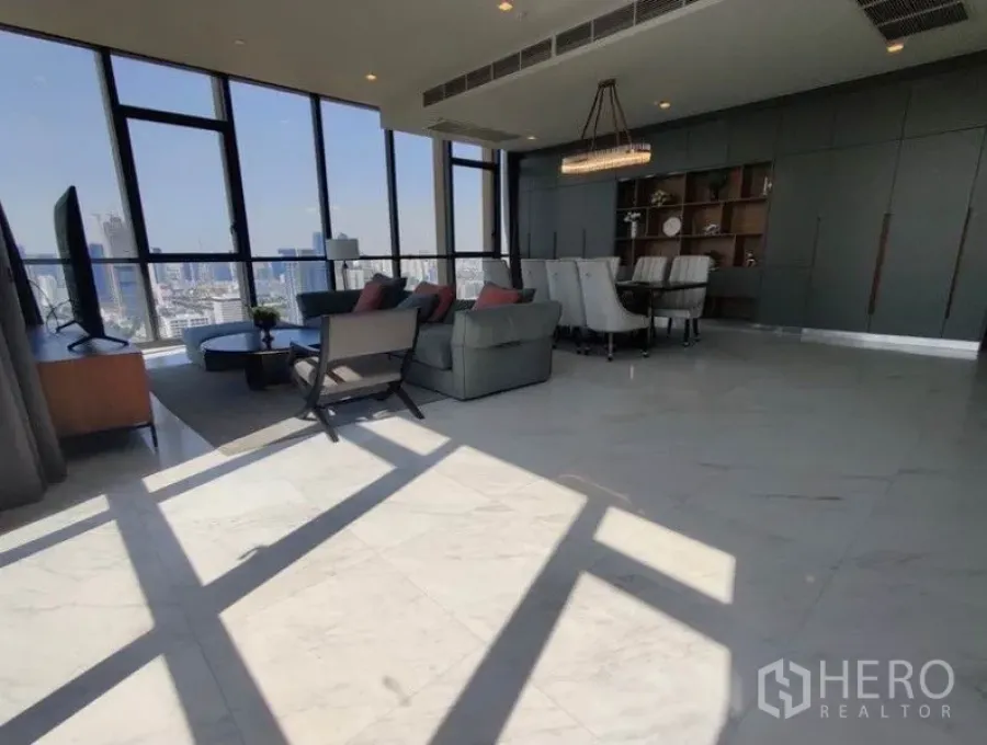 Condominium for rent in Watthana, Bangkok - Sun-filled living and dining room with marble floors, sofa set, chandelier, and floor-to-ceiling windows overlooking the Bangkok skyline.