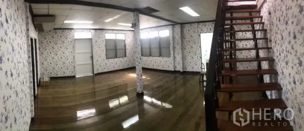 Detached House for rent in Sathon, Bangkok - Spacious living area with polished wooden floors, floral wallpaper and a wooden staircase.