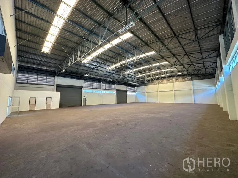 Factory for rent in Chon Buri - Open production hall featuring multiple roller shutter doors, high ceilings, and a clean concrete floor.