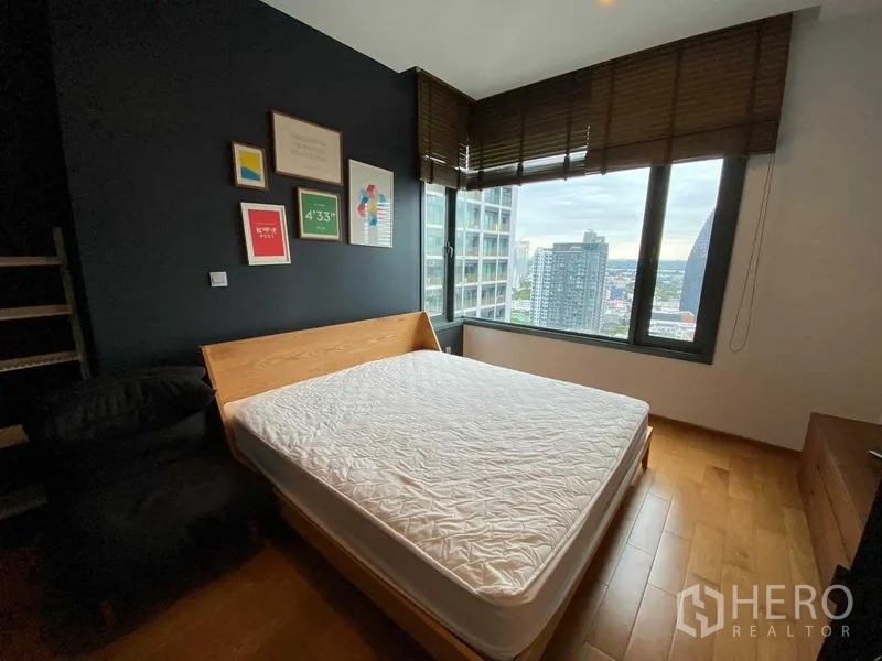 Condominium for rent in Khlong Toei, Bangkok - Corner bedroom with wood bed frame, dark accent wall and large window overlooking the skyline.