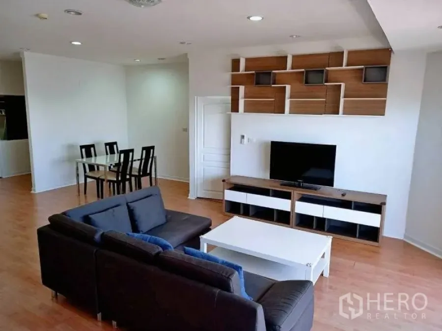 Condominium for rent in Khlong Toei, Bangkok - Open-plan living room with dark sofa, TV console and geometric wall shelves on wood floors.