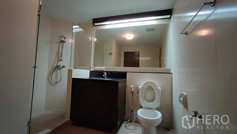 Condominium for rent in Khlong Toei, Bangkok - Modern bathroom featuring a glass-enclosed shower, large mirror, vanity and toilet.