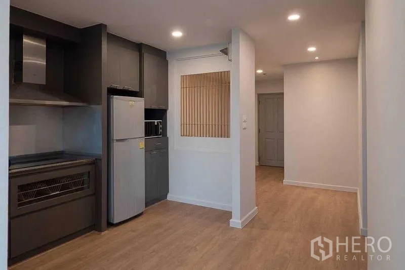 Condominium for sale in Chatuchak, Bangkok - Modern kitchen with dark cabinetry, stainless appliances and adjoining hallway.