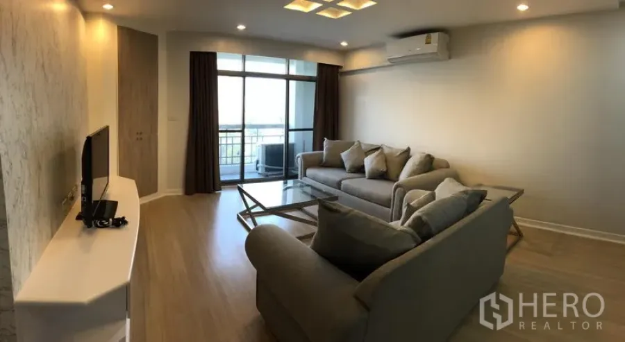 Condominium for rent in Watthana, Bangkok - Living area with sofa set, TV stand, ceiling lights and sliding doors opening to a balcony.