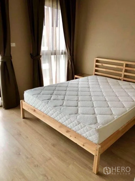 Townhouse for rent in Suan Luang, Bangkok - Bright bedroom with wooden bed frame, large windows and dark drapes on wood floors.