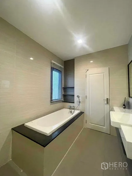 Detached House for sale in Bang Kruai, Nonthaburi - Bright bathroom featuring a built‑in bathtub, window with blinds and a sleek vanity in neutral tiles.