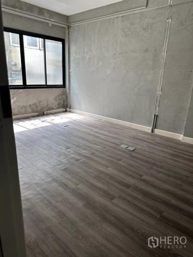 Shophouse for sale in Watthana, Bangkok - Concrete-finish room with a wide window and wood-look flooring.