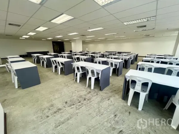 Office Space for rent - Spacious office area with multiple tables, central column, bright lighting and exposed concrete flooring.