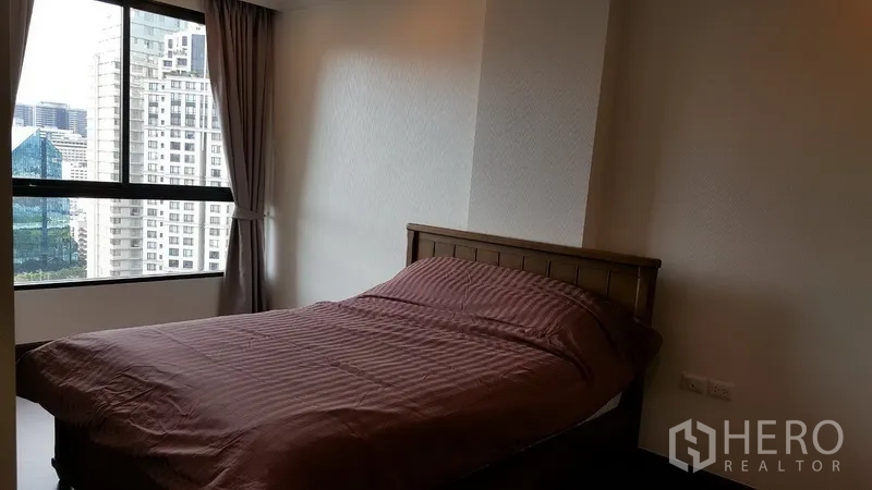 Condominium for rent in Sathon, Bangkok - Bright bedroom with large window and city view, queen bed and curtains.