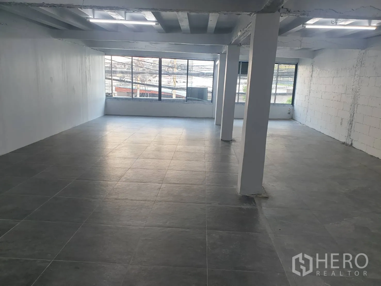 Retail Space for rent in Khlong Toei, Bangkok - Large open retail area with multiple pillars, grey tiles and floor-to-ceiling windows bringing natural light.