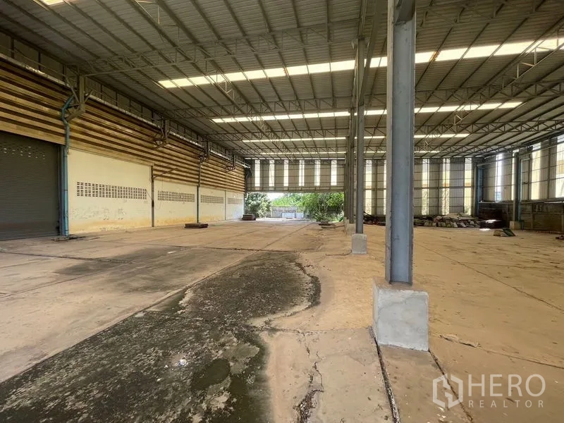 Warehouse for rent or sale in Bang Bon, Bangkok - Open production area with steel columns, a loading bay opening, and a partially wet floor.
